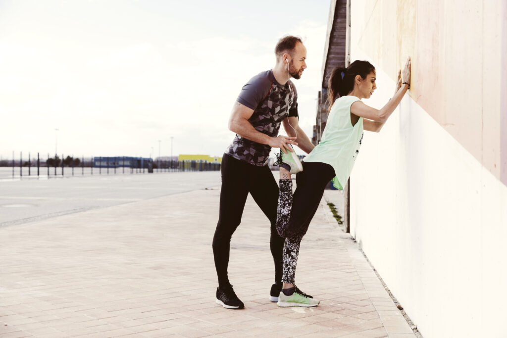 male-trainer-assisting-female-athlete-while-stretching