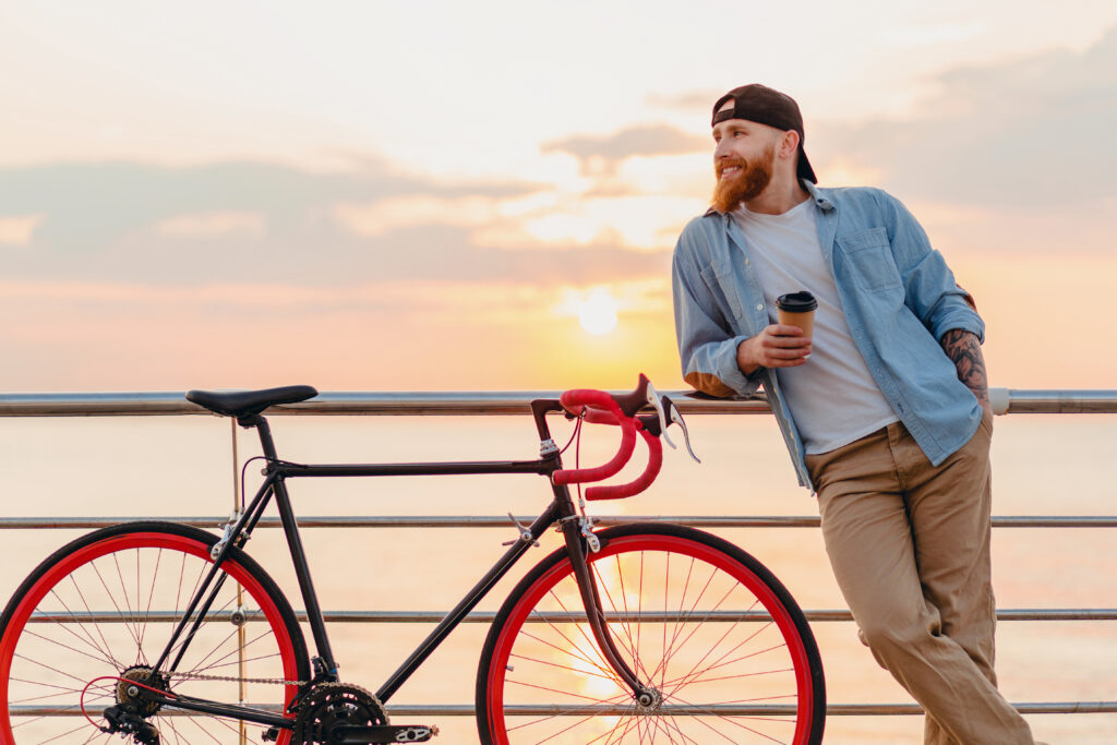 young bearded man traveling on bicycle at sunset sea